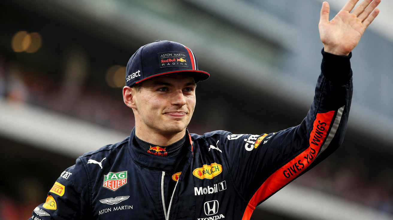 Piloto de Fórmula 1 com macacão da Red Bull Racing a acenar com a mão direita.