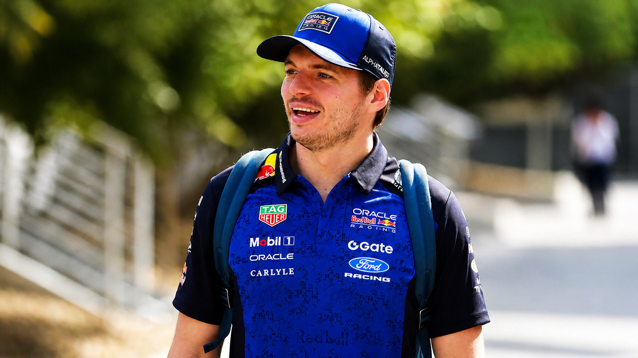 Homem jovem com boné azul e uniforme da equipa AlphaTauri sorrindo ao ar livre.