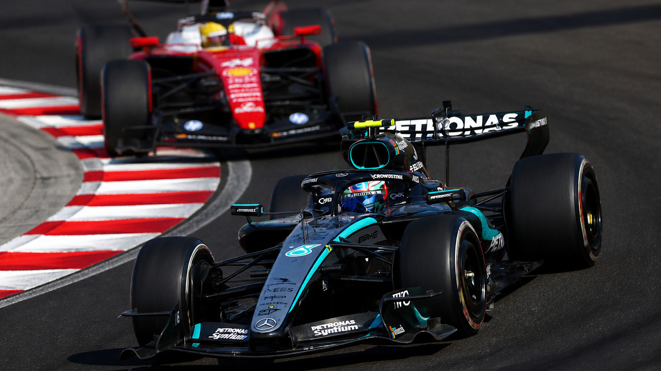 Dois carros de Fórmula 1 em curva numa pista, com destaque para o carro preto da Mercedes à frente.
