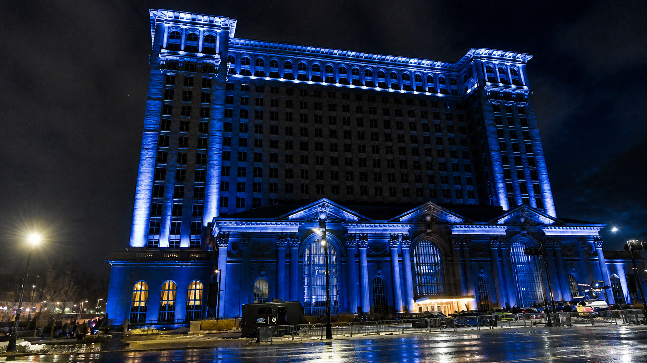 Edifício grande iluminado com luzes azuis durante a noite, refletindo-se no chão molhado.