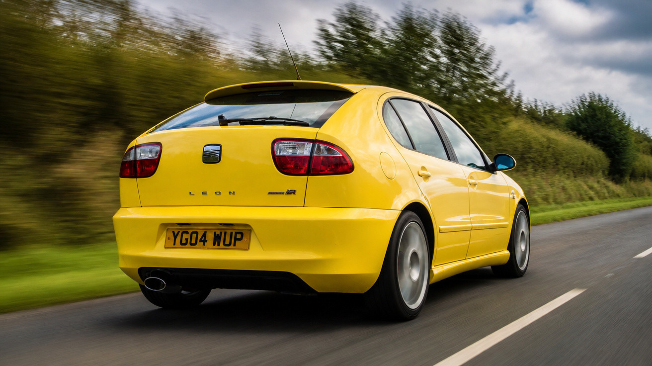 Carro amarelo Seat Leon em estrada rural, a alta velocidade, sob céu nublado.
