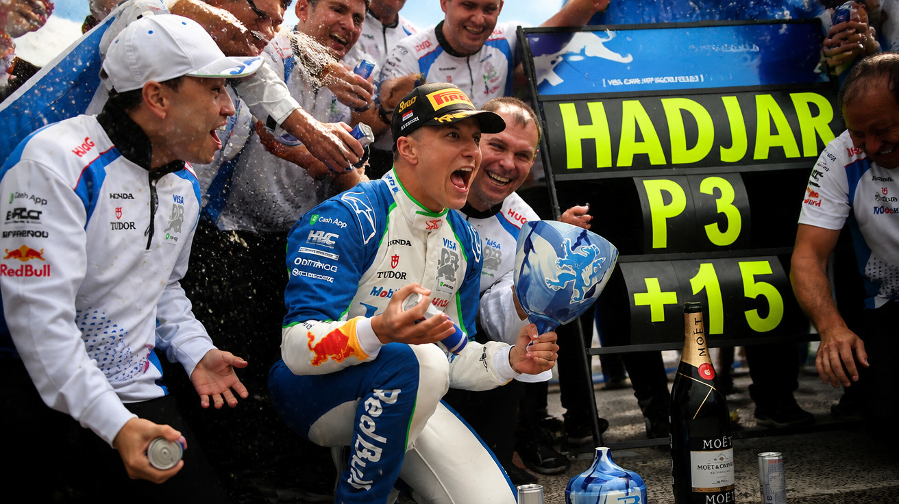 Piloto de corridas celebra com equipa após conquista do 3º lugar, rodeados por champanhe e troféus.